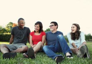 Two young adult couples sitting in the grass talking and enjoying each other's friendship.