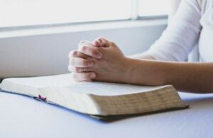 Person with hands folded on an open Bible and praying.