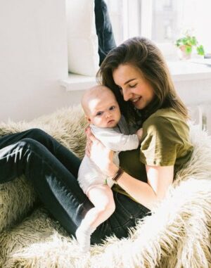 Young woman sitting on a large chair holding her 6 month old baby.