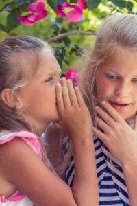 Young girl whispering in ear of girl