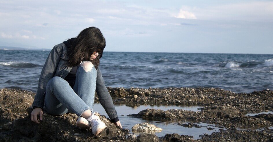 Woman thinking as she sits on rocks beside ocean